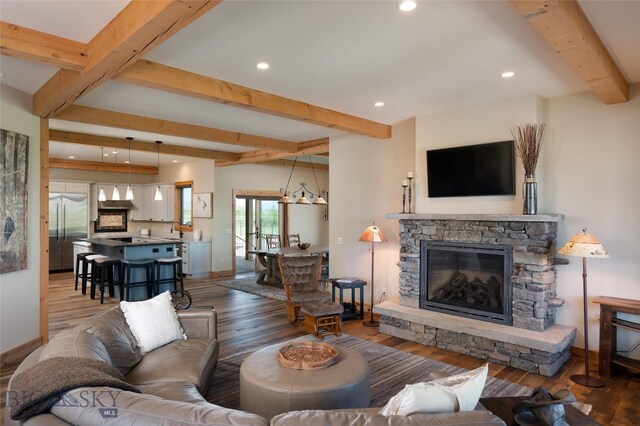 living room featuring hardwood / wood-style floors, sink, beam ceiling, and a stone fireplace