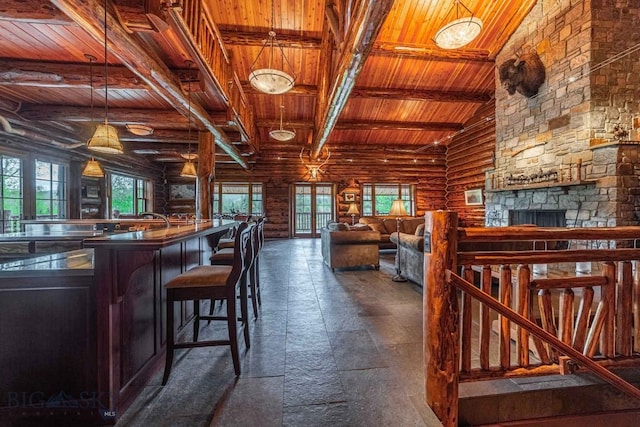 interior space featuring a stone fireplace, hanging light fixtures, lofted ceiling with beams, wooden ceiling, and log walls