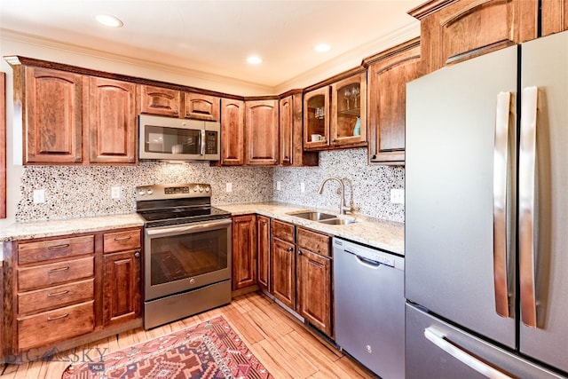 kitchen with light hardwood / wood-style flooring, stainless steel appliances, sink, light stone counters, and tasteful backsplash