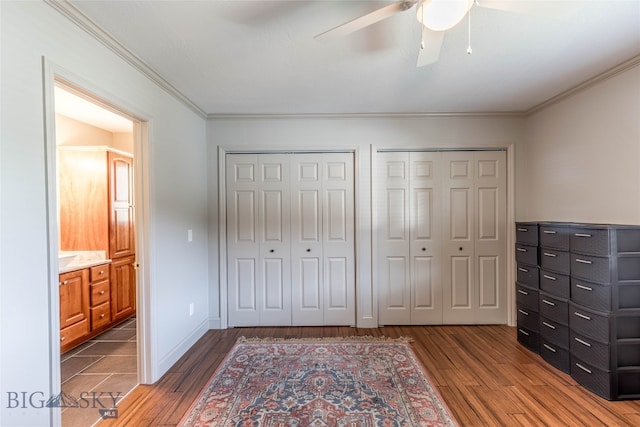 unfurnished bedroom featuring ornamental molding, wood-type flooring, ceiling fan, and multiple closets