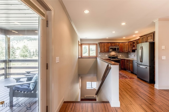 kitchen featuring a baseboard heating unit, stainless steel appliances, crown molding, tasteful backsplash, and hardwood / wood-style flooring