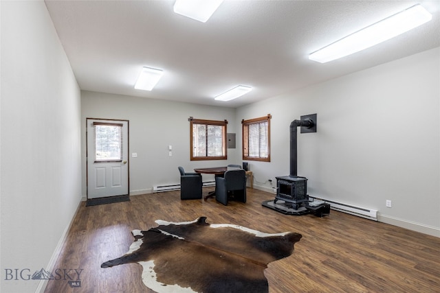 home office featuring a wood stove, baseboard heating, and dark wood-type flooring