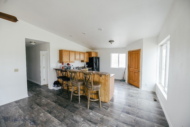 kitchen featuring tile flooring, a breakfast bar, black fridge with ice dispenser, lofted ceiling, and kitchen peninsula