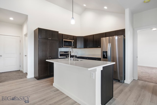 kitchen featuring pendant lighting, high vaulted ceiling, light hardwood / wood-style flooring, stainless steel appliances, and an island with sink