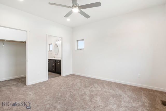 unfurnished bedroom featuring a closet, light carpet, connected bathroom, sink, and ceiling fan