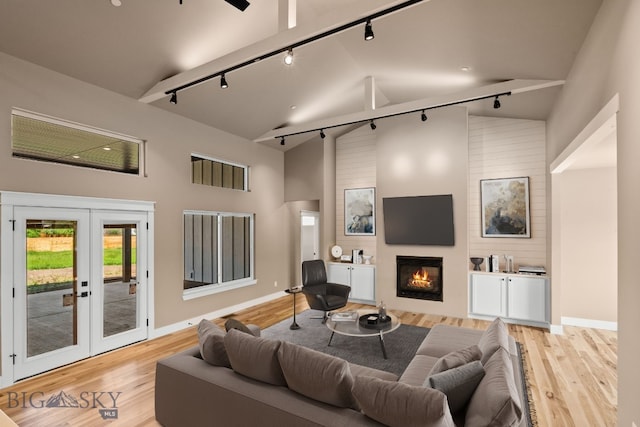 living room featuring light wood finished floors, high vaulted ceiling, french doors, and a glass covered fireplace