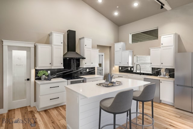 kitchen with sink, appliances with stainless steel finishes, white cabinetry, a center island, and wall chimney exhaust hood