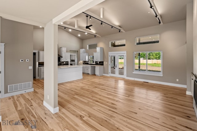 unfurnished living room featuring a high ceiling, visible vents, baseboards, light wood finished floors, and track lighting