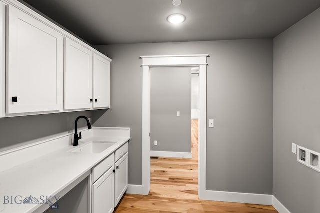 clothes washing area with cabinets, sink, washer hookup, and light hardwood / wood-style floors