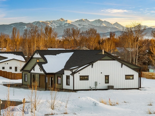 snow covered property with board and batten siding, fence, and a mountain view