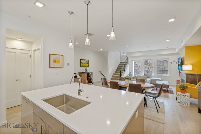 kitchen with hanging light fixtures, sink, light hardwood / wood-style floors, and an island with sink