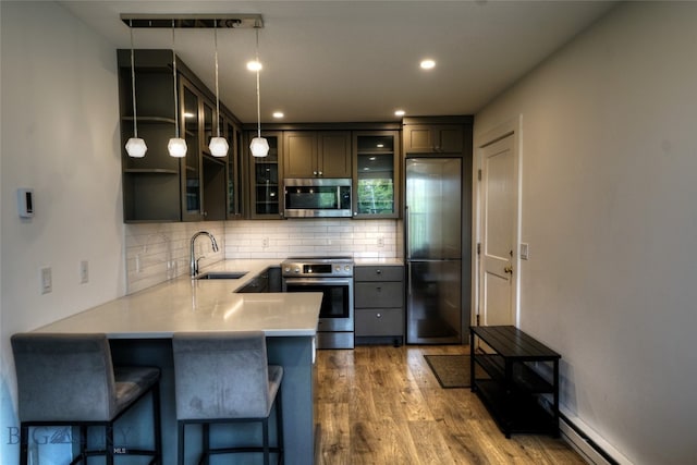 kitchen with hanging light fixtures, hardwood / wood-style flooring, stainless steel appliances, sink, and kitchen peninsula