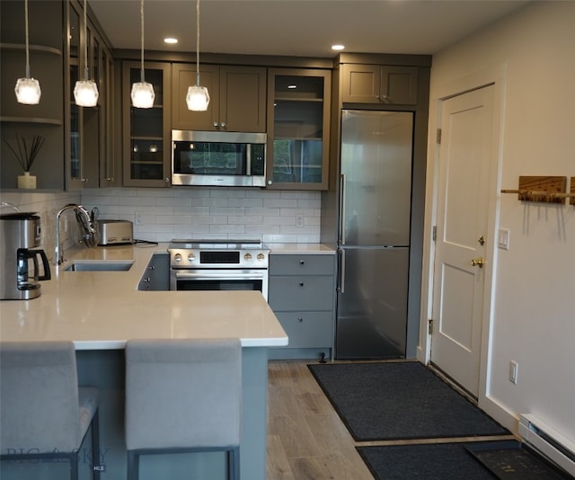 kitchen with a baseboard radiator, hardwood / wood-style floors, stainless steel appliances, sink, and kitchen peninsula