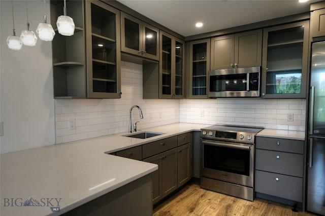 kitchen with pendant lighting, light hardwood / wood-style flooring, stainless steel appliances, sink, and decorative backsplash