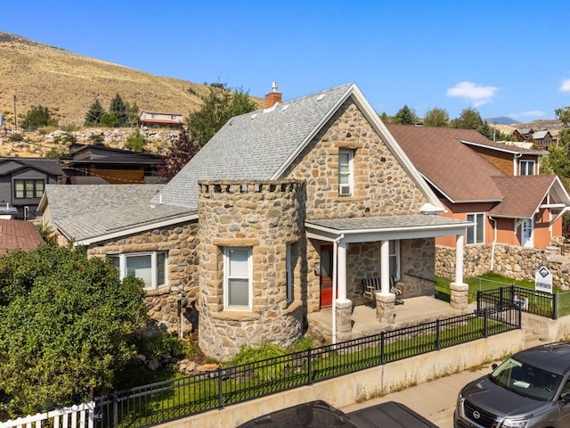 view of front facade featuring stone siding, a fenced front yard, a chimney, and a shingled roof