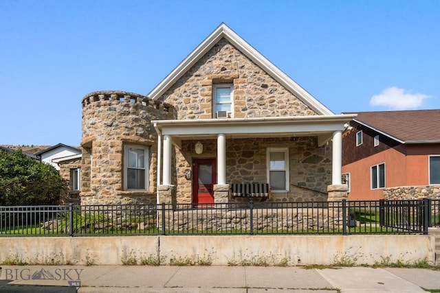 view of front of house featuring stone siding, a fenced front yard, and covered porch