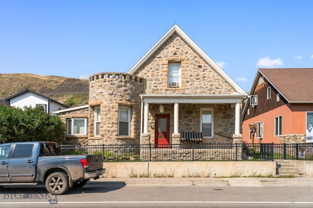 view of front of home with a fenced front yard, covered porch, a mountain view, and stone siding