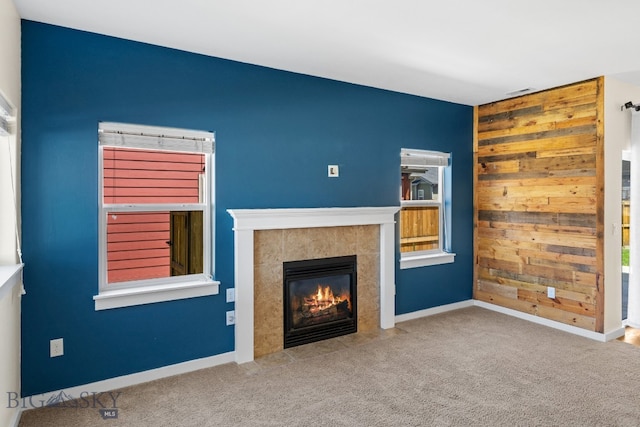 unfurnished living room with a fireplace, carpet floors, and wood walls