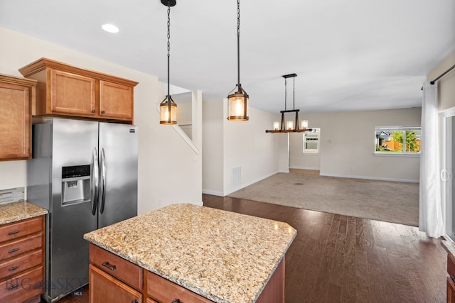 kitchen featuring light stone counters, a kitchen island, pendant lighting, and stainless steel refrigerator with ice dispenser