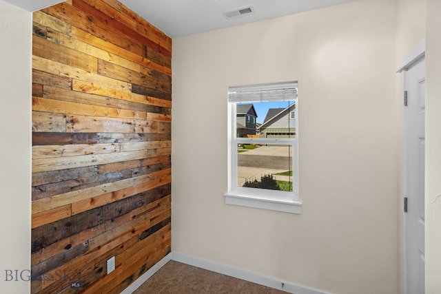 empty room with dark tile patterned floors, a wealth of natural light, and wooden walls