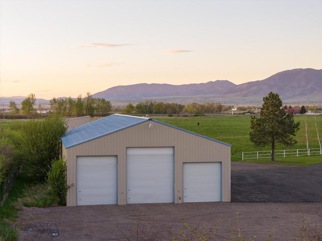 garage at dusk with a detached garage, a mountain view, and fence