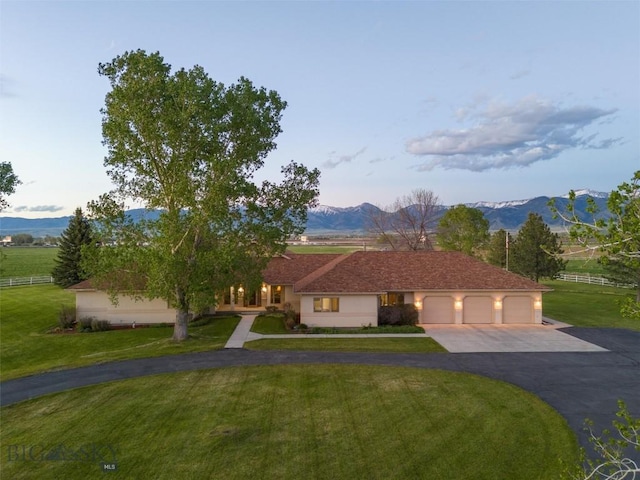 view of front of house with an attached garage, fence, a mountain view, driveway, and a front lawn