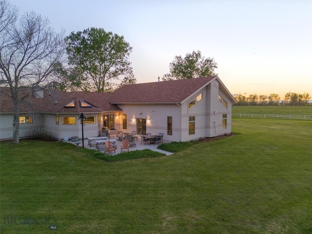 rear view of house with stucco siding, a patio, fence, and a lawn