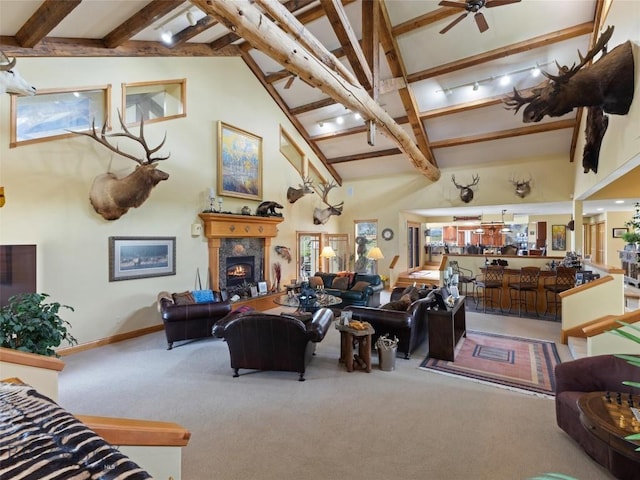 living area with a warm lit fireplace, ceiling fan, beamed ceiling, carpet, and high vaulted ceiling