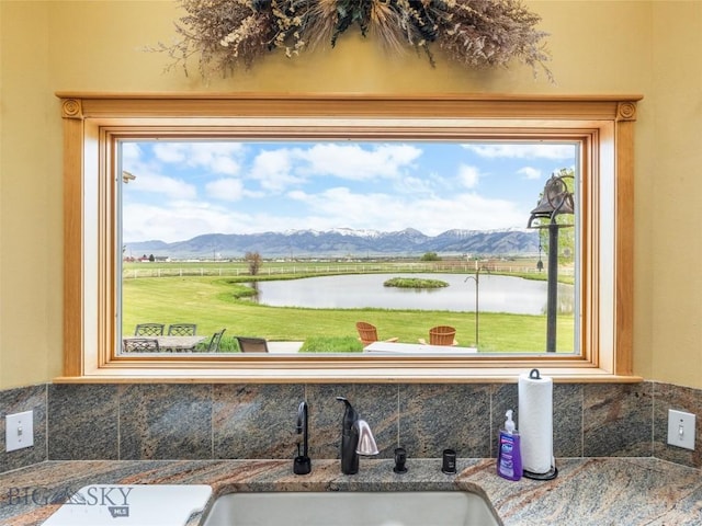 interior details with a water and mountain view, decorative backsplash, and a sink