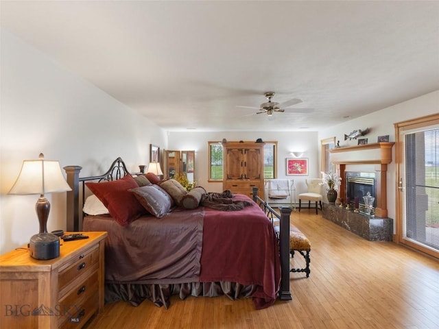 bedroom with a fireplace, light wood finished floors, and ceiling fan