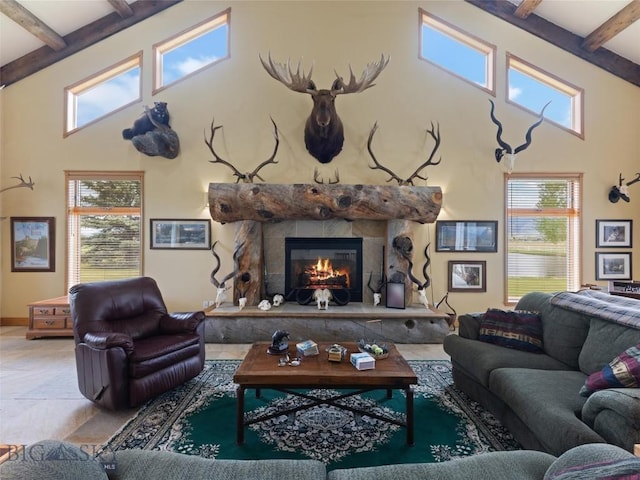 living room featuring beam ceiling, a high ceiling, a wealth of natural light, and a glass covered fireplace