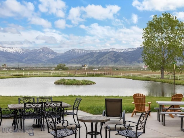 view of property's community with outdoor dining area, a patio, fence, and a water and mountain view