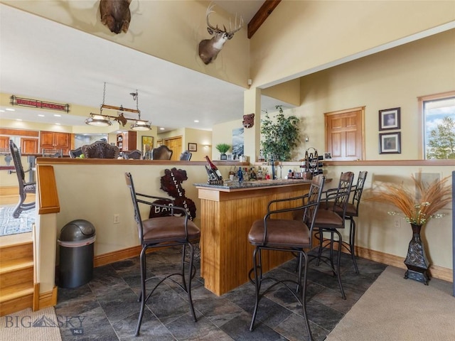 bar with stone finish floor, a towering ceiling, and baseboards