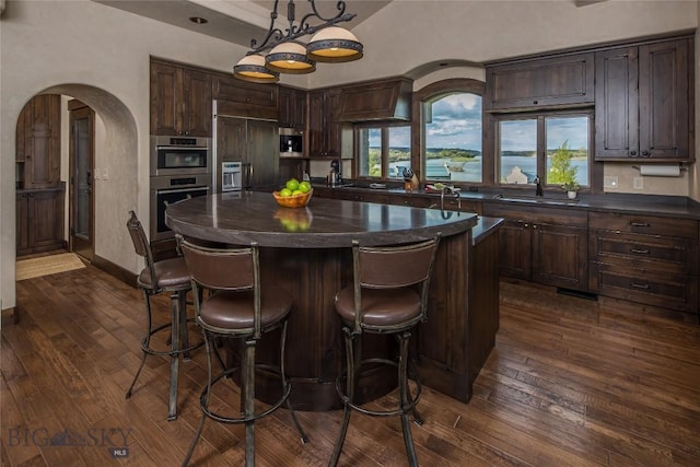 kitchen with pendant lighting, a center island, stainless steel double oven, and dark brown cabinetry