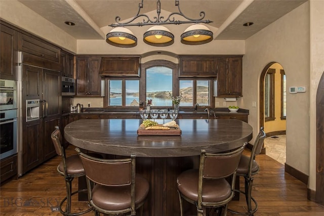 kitchen with stainless steel double oven, dark brown cabinetry, dark hardwood / wood-style floors, and a center island