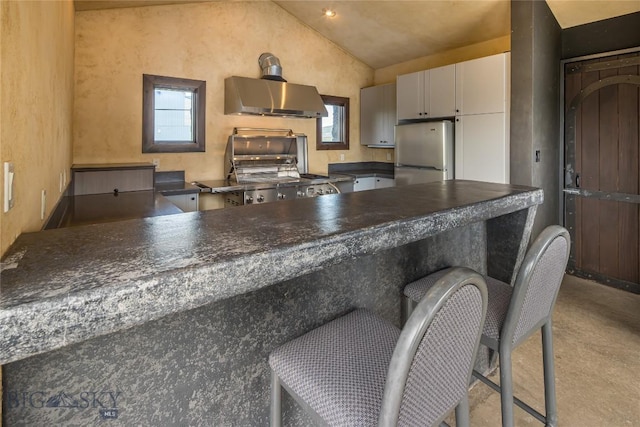 kitchen featuring stainless steel fridge, stove, gray cabinetry, wall chimney exhaust hood, and lofted ceiling