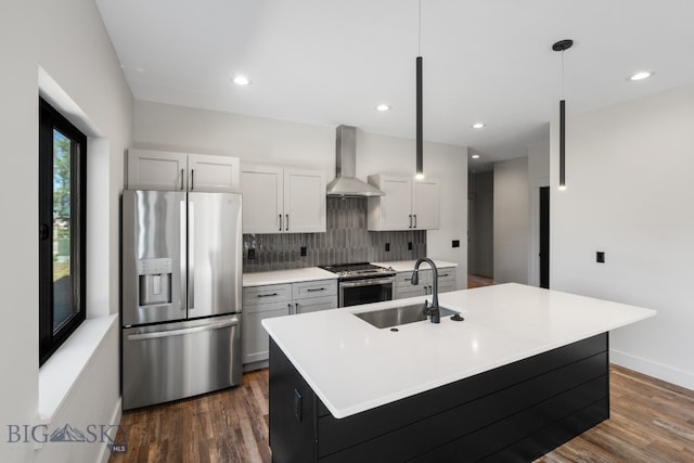 kitchen featuring decorative light fixtures, backsplash, wall chimney exhaust hood, a kitchen island with sink, and appliances with stainless steel finishes