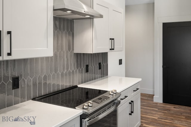 kitchen featuring wall chimney range hood, backsplash, dark wood-type flooring, white cabinets, and electric stove