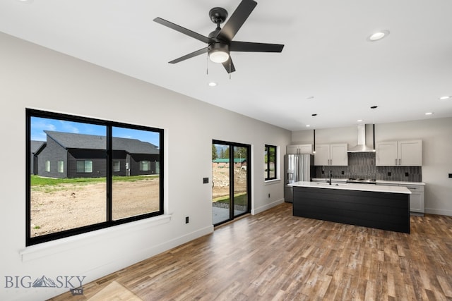 kitchen with decorative light fixtures, backsplash, a center island with sink, wall chimney exhaust hood, and wood-type flooring