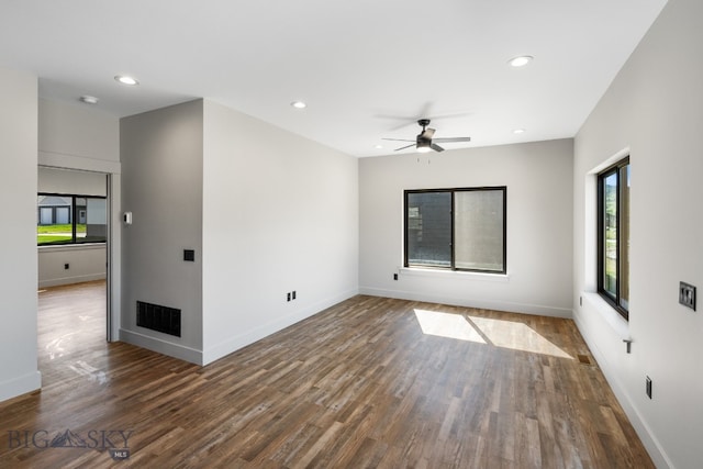 unfurnished room featuring a healthy amount of sunlight, ceiling fan, and dark hardwood / wood-style flooring