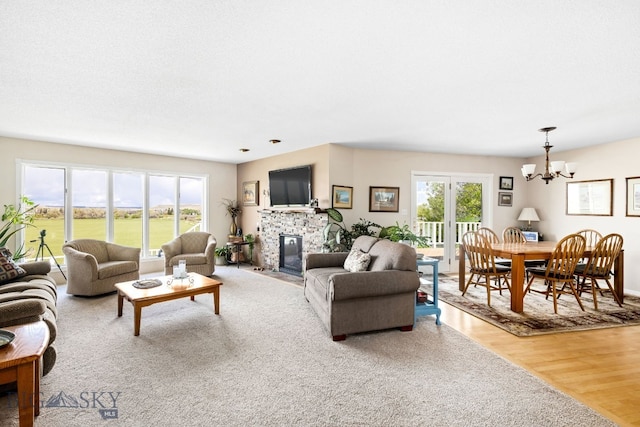 living room with hardwood / wood-style floors, a stone fireplace, and an inviting chandelier