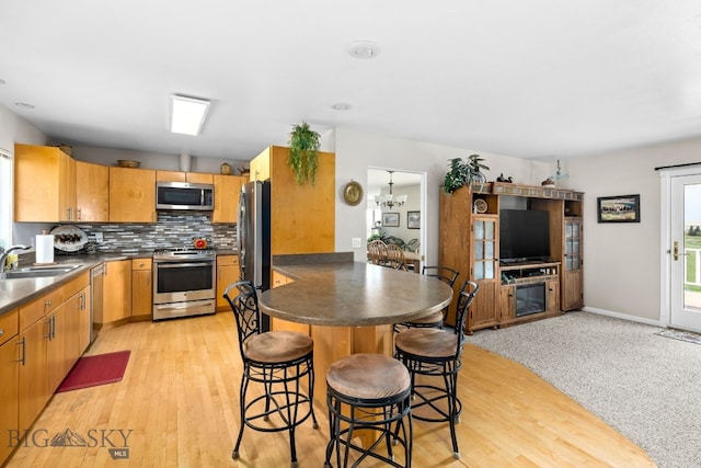 kitchen featuring an inviting chandelier, sink, light hardwood / wood-style flooring, appliances with stainless steel finishes, and tasteful backsplash