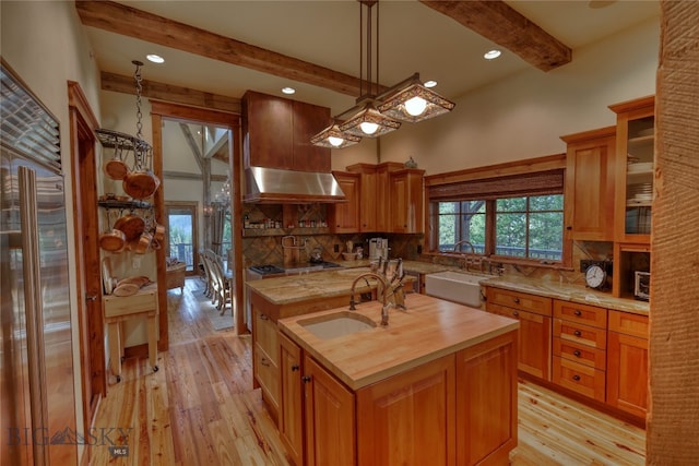 kitchen featuring light hardwood / wood-style flooring, backsplash, an island with sink, beamed ceiling, and sink