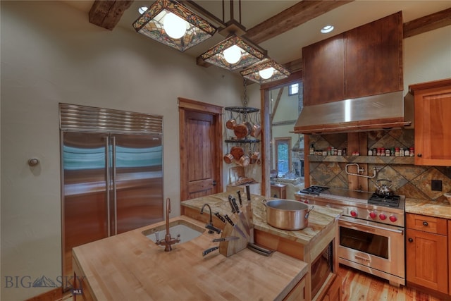 kitchen with backsplash, built in appliances, wall chimney exhaust hood, light wood-type flooring, and sink