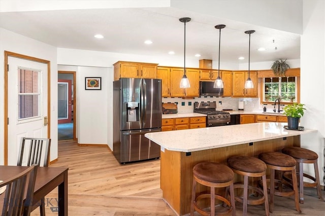 kitchen featuring light wood-type flooring, stainless steel appliances, kitchen peninsula, decorative light fixtures, and backsplash