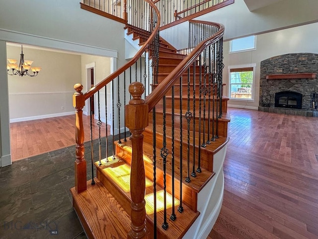 stairs featuring hardwood / wood-style flooring, an inviting chandelier, a fireplace, baseboards, and a towering ceiling