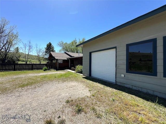 view of property exterior featuring a garage, dirt driveway, and fence