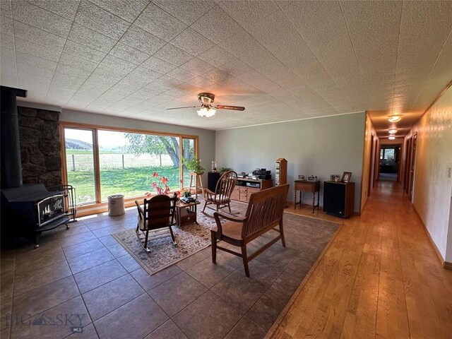 living area with a ceiling fan, wood finished floors, and a wood stove