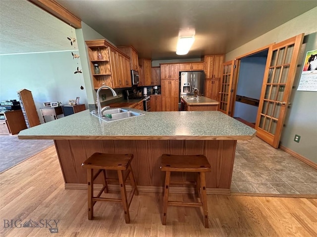 kitchen featuring brown cabinets, open shelves, appliances with stainless steel finishes, a sink, and a peninsula