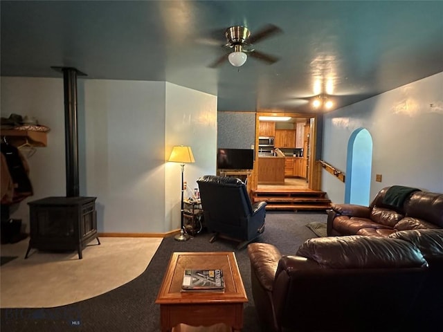 carpeted living area with arched walkways, a ceiling fan, and a wood stove